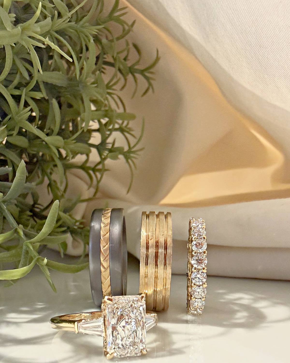Four custom wedding and engagement rings on a cream backdrop